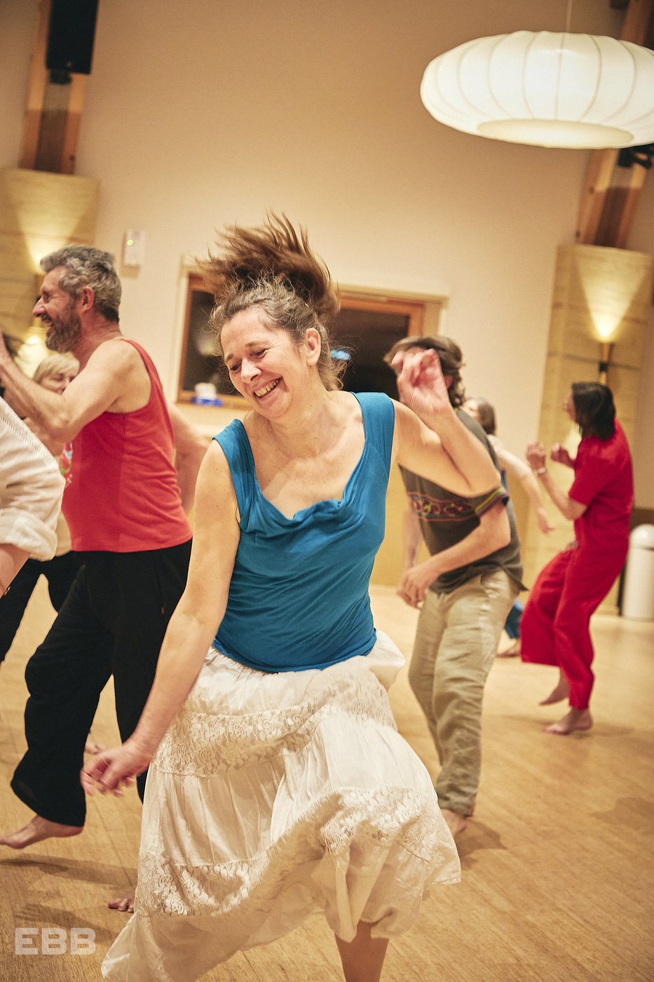 Une danseuse en mouvement, cheveux au vent et sourire radieux, dans une salle de Biodanza
