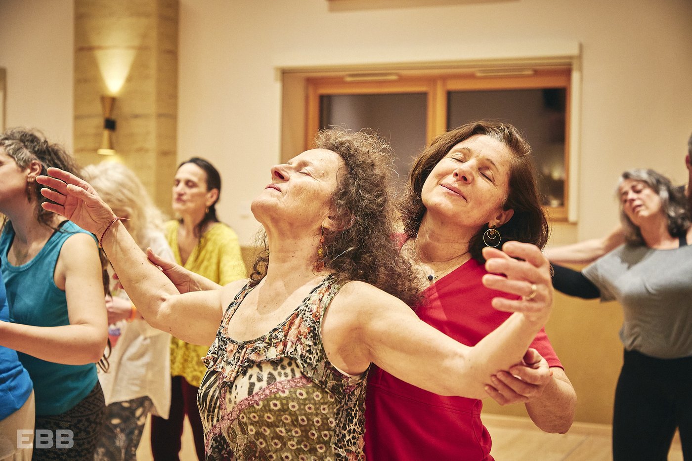 Des participantes les yeux fermés, bras ouverts dans un mouvement lent et apaisant, dans une salle de Biodanza